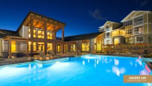 A modern apartment complex at night features a brightly lit outdoor swimming pool, lounge chairs, and large windows. A sign reads ASCENT 430 Wexford, PA in the lower right corner.