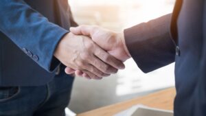 Two people in business attire shaking hands, suggesting agreement or partnership, with a bright, blurred office background.