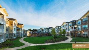 Modern apartment buildings surround a well-maintained green courtyard with winding sidewalks, landscaping, and a clear blue sky. A sign in the corner reads Ascent 430, Wexford, PA.