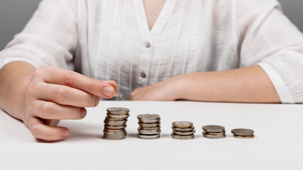 A person in a white shirt stacks and arranges coins in ascending order on a white table, illustrating the concept of saving or financial growth.
