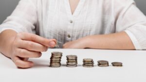 A person in a white shirt stacks and arranges coins in ascending order on a white table, illustrating the concept of saving or financial growth.