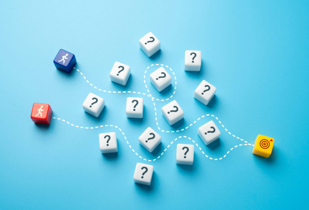 White dice with question marks are scattered on a blue surface. Dotted lines connect a starting block with a running figure to a target block with a bullseye, illustrating multiple possible paths and decisions.