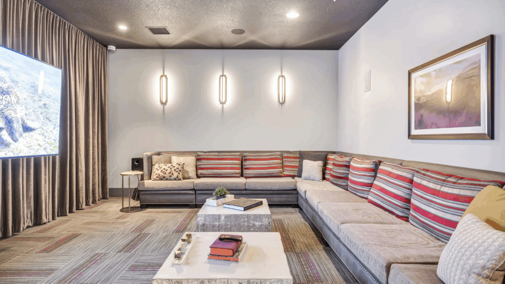 A modern lounge with an L-shaped sofa featuring striped cushions, a large wall-mounted TV, two marble coffee tables, wall art, three vertical lights, and floor-to-ceiling curtains.