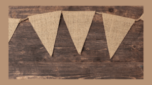 Burlap pennant flags hang on a string against a rustic wooden background, with a brown border framing the image.