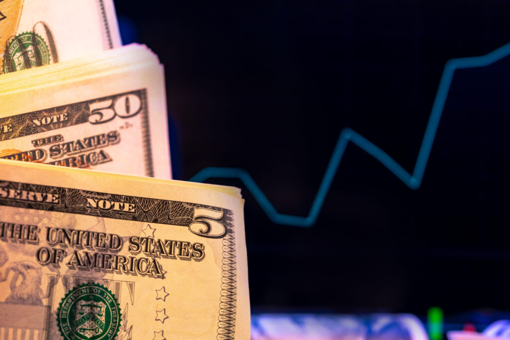 Close-up of U.S. five and fifty dollar bills with a blurred line graph in the background, suggesting financial growth or economic trends.