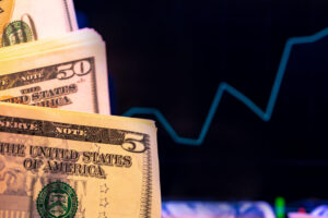 Close-up of U.S. five and fifty dollar bills with a blurred line graph in the background, suggesting financial growth or economic trends.
