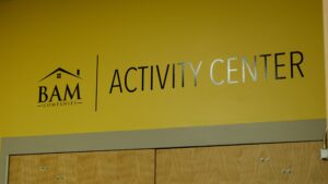 Yellow wall with BAM Companies Activity Center written in black and silver letters above light wooden double doors.