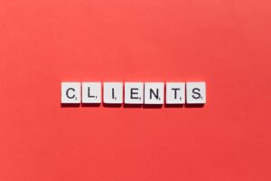 Scrabble tiles spelling out CLIENTS are arranged in a row on a bright red background.