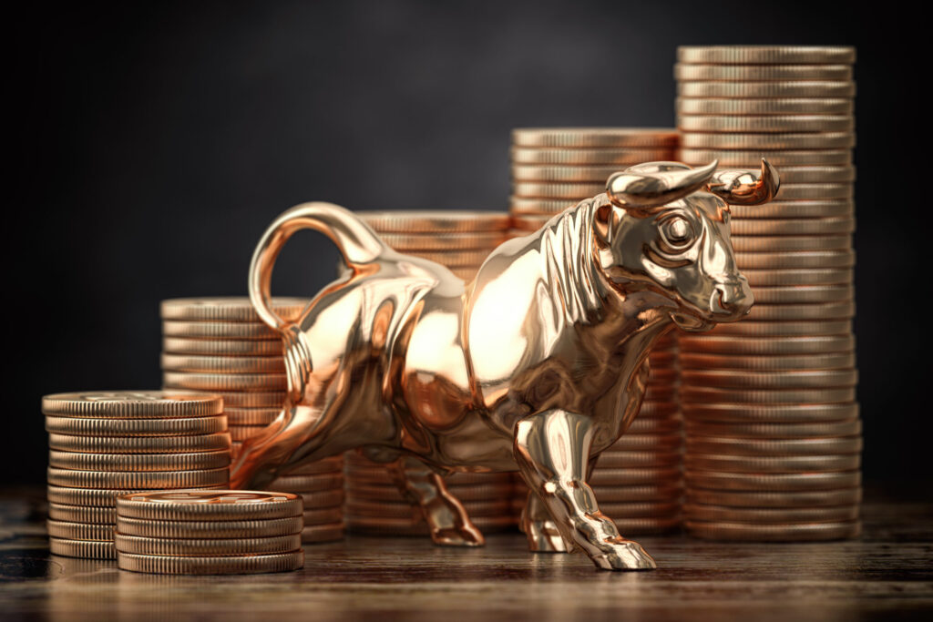 A shiny golden bull figurine stands in front of several stacks of gold coins on a wooden surface, symbolizing financial growth, prosperity, or a bullish market trend.
