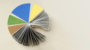 A pie chart with colorful segments, with one segment replaced by a fanned-out stack of U.S. dollar bills, illustrating the concept of financial distribution or budget allocation.