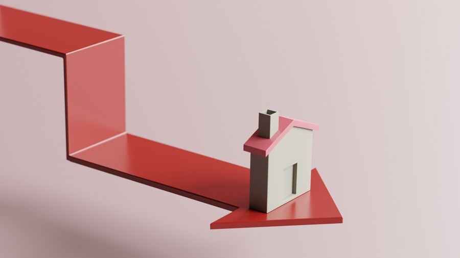 A small house model sits on a red downward-pointing arrow, symbolizing a decline, against a pale pink background. The image visually conveys the concept of falling real estate or housing market values.